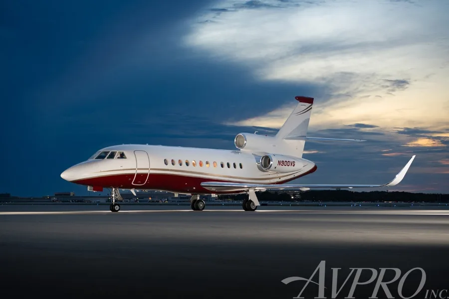 A Dassault Falcon 900EX business jet with a white and red paint scheme on the tarmac at sunset.