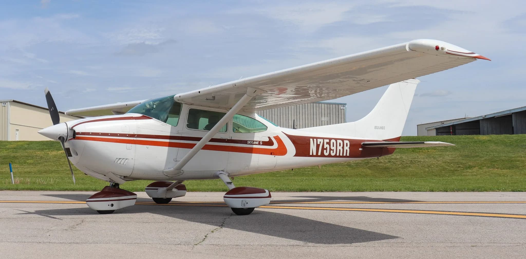 A white and brown Cessna Skylane S (N759RR) parked on an asphalt ramp with hangars in the background.