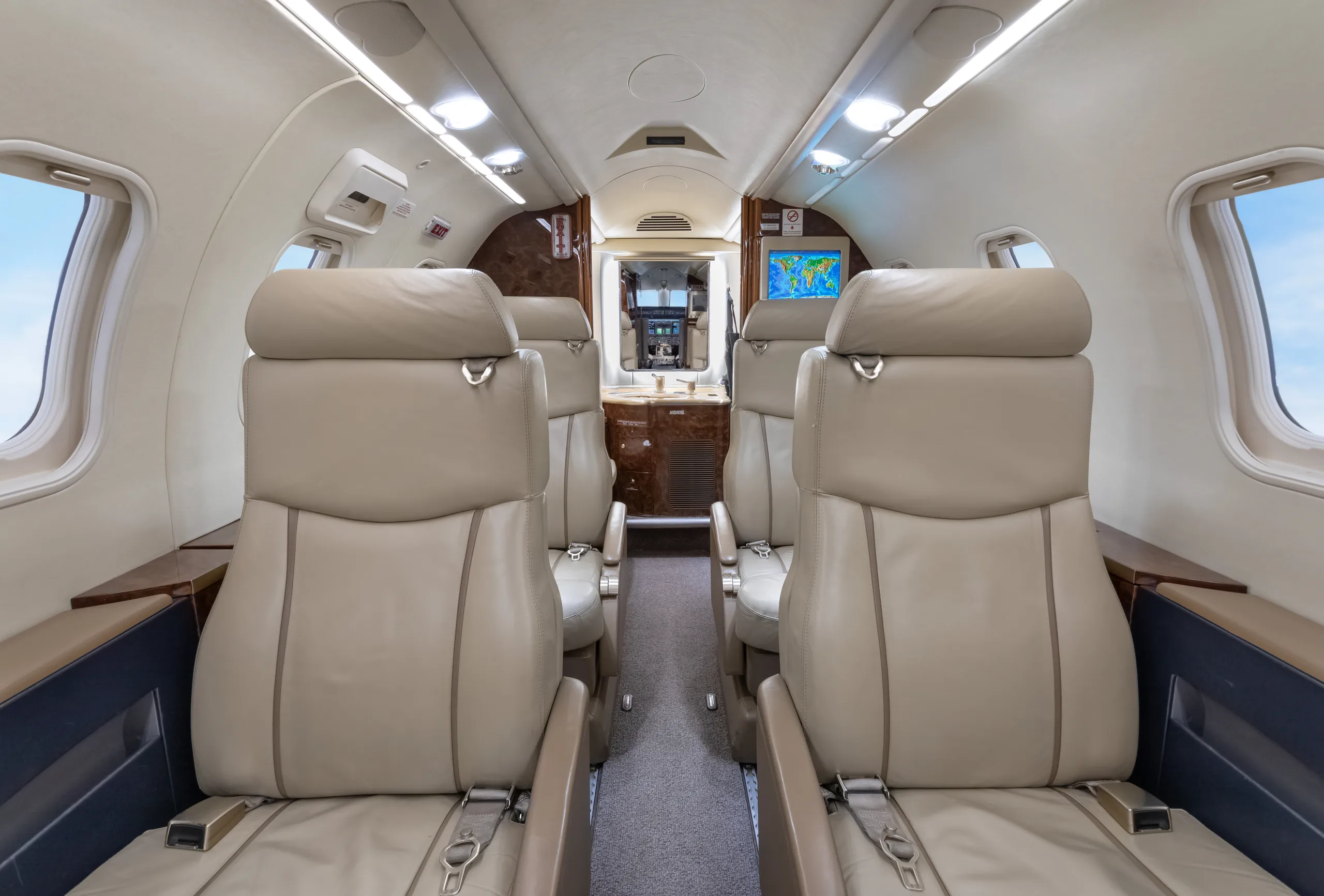 The elegant cabin interior of a private jet, showing rows of beige leather seats and a world map displayed on a screen at the front.