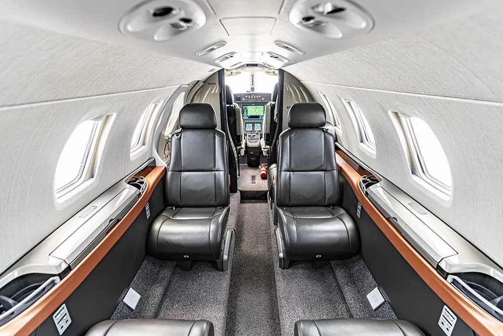 The aircraft cabin interior with two rows of dark leather seats and a view towards the cockpit.