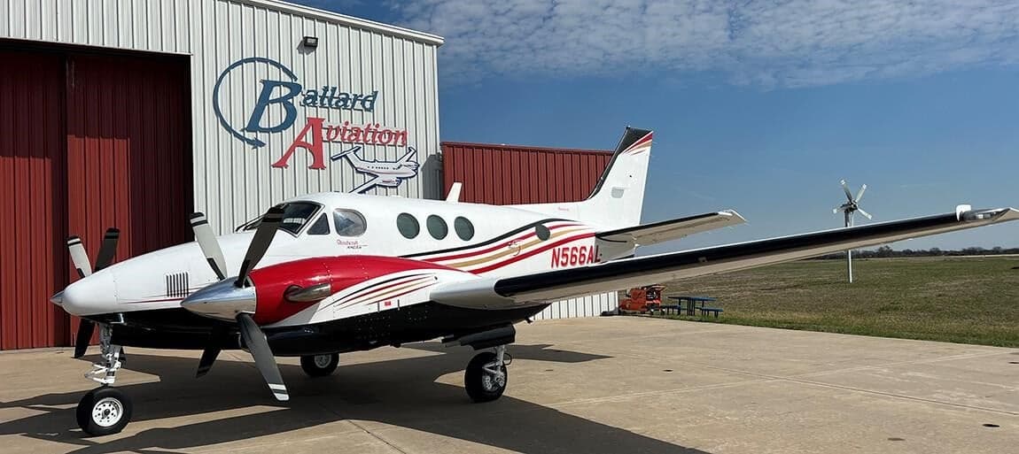 King Air aircraft with red and gold paint scheme parked in front of a hangar.