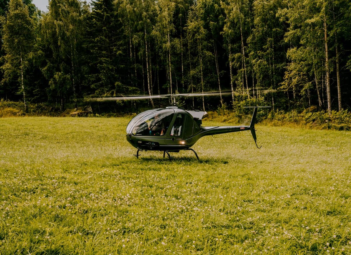 Helicopter landing in a grassy field surrounded by trees.
