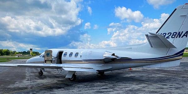 A white Cessna Citation jet with an open door is parked on the tarmac.
