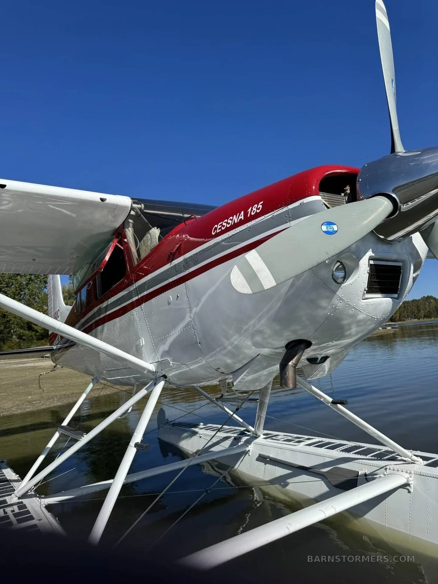 A close-up view of the red and white nose and floats of a Cessna 185 seaplane on the water.