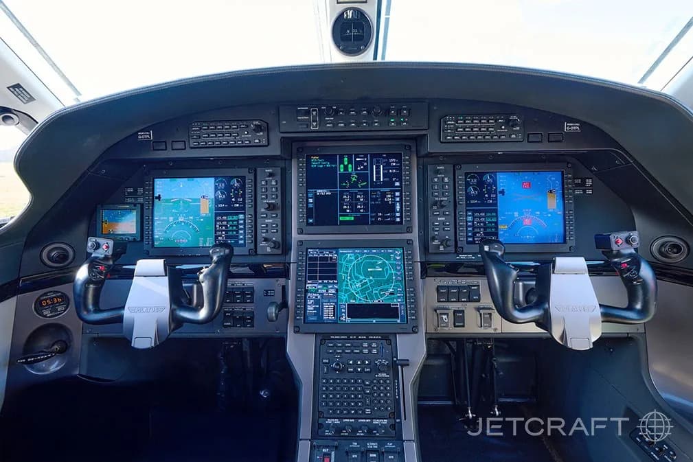 The modern glass cockpit of a Pilatus PC-12 with multiple digital displays and two control yokes.