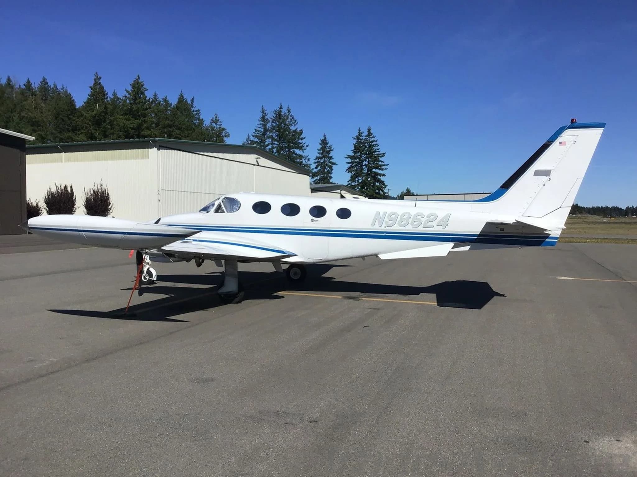 A white and blue twin-engine Cessna 340 aircraft, N98624, parked on an airfield next to a hangar.