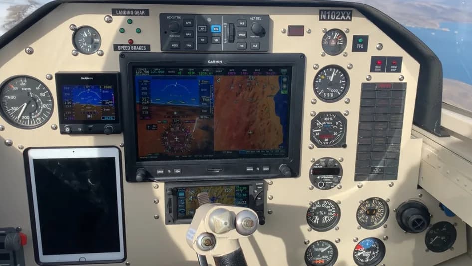 The cockpit instrument panel of an aircraft, featuring multiple gauges, two large Garmin displays, and an iPad mounted on the left.