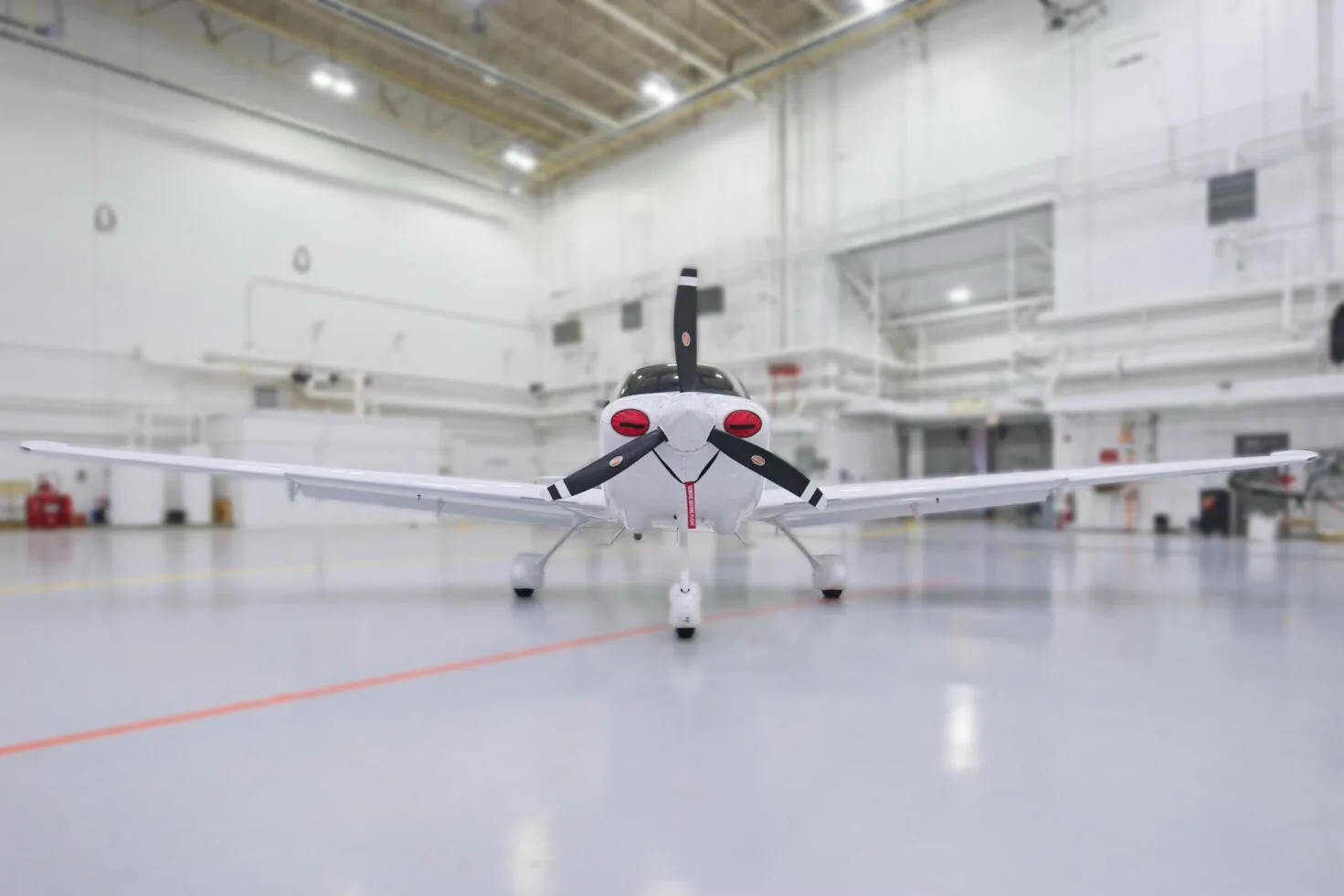 A head-on view of a white Cirrus SR22 aircraft with a black propeller and red propeller covers, N322NE, in a hangar.