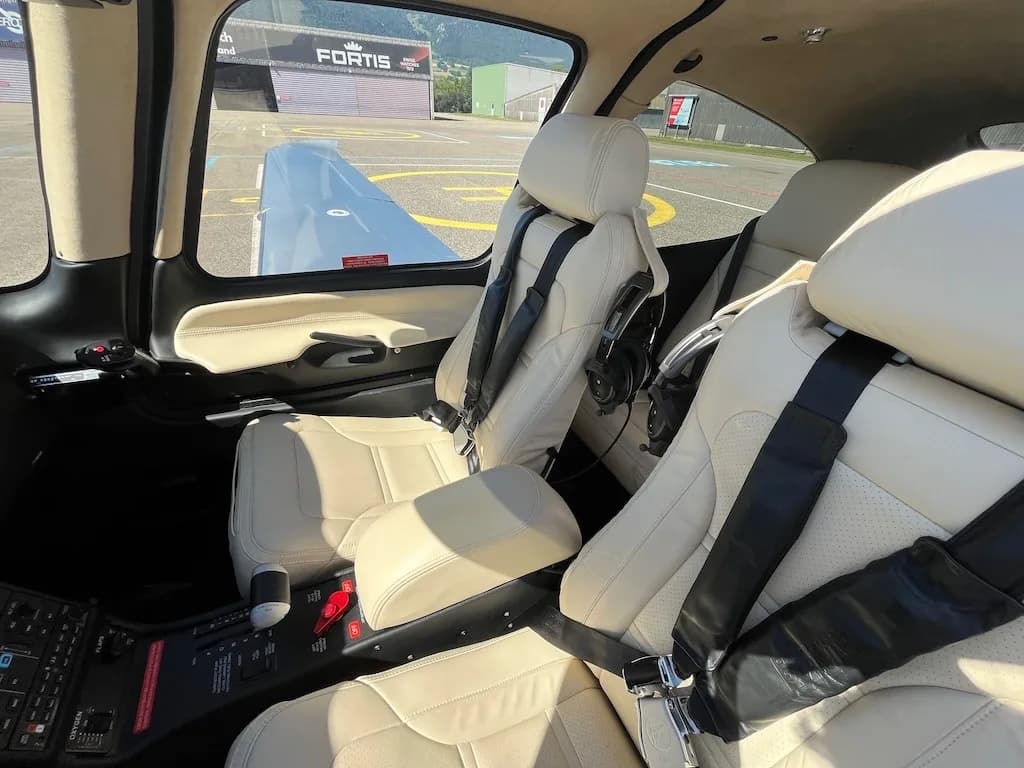 Interior view of the aircraft cabin with light-colored leather seats and black seatbelts.