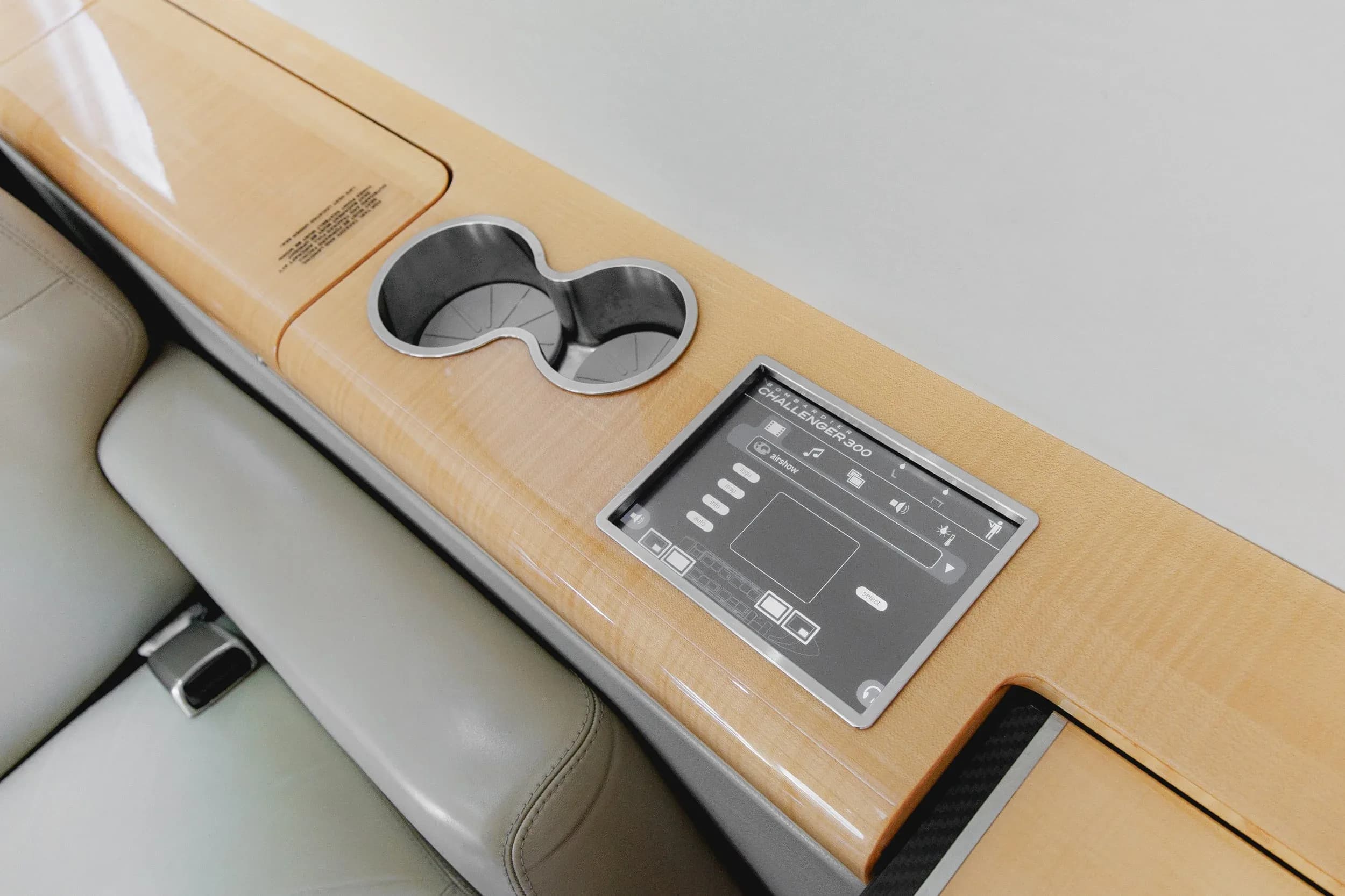 A close-up of a control panel and two cup holders integrated into the light wood side panel of a private jet cabin.