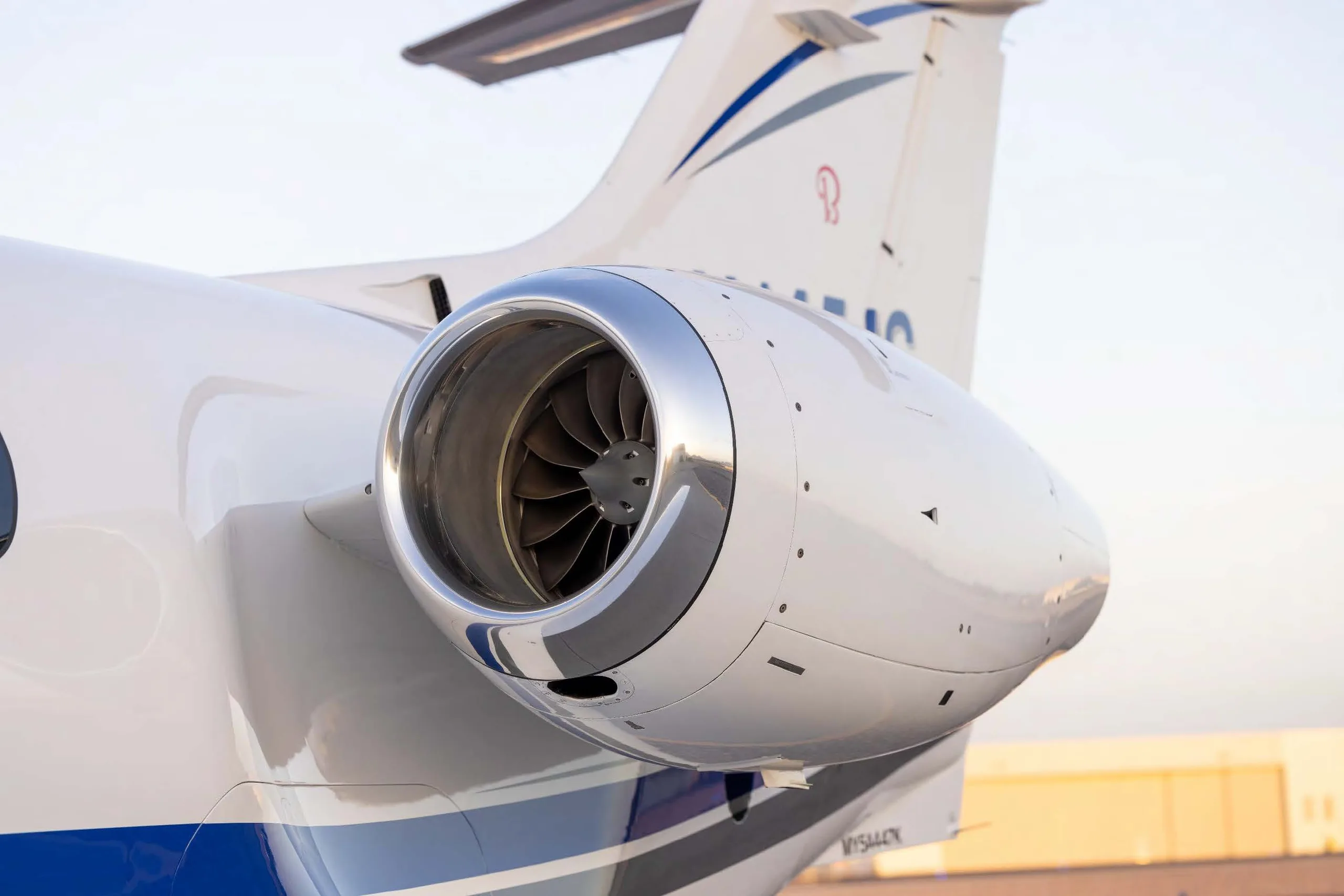 A close-up view of the rear fuselage and engine of a white business jet with blue accents on the tail.