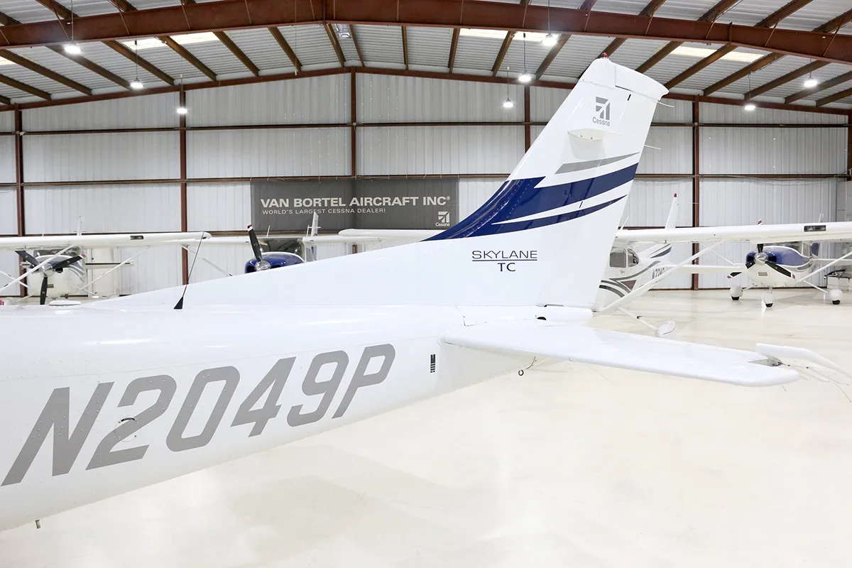 Close-up of the tail section of a white and blue Cessna Skylane TC (N2049P) in a hangar.