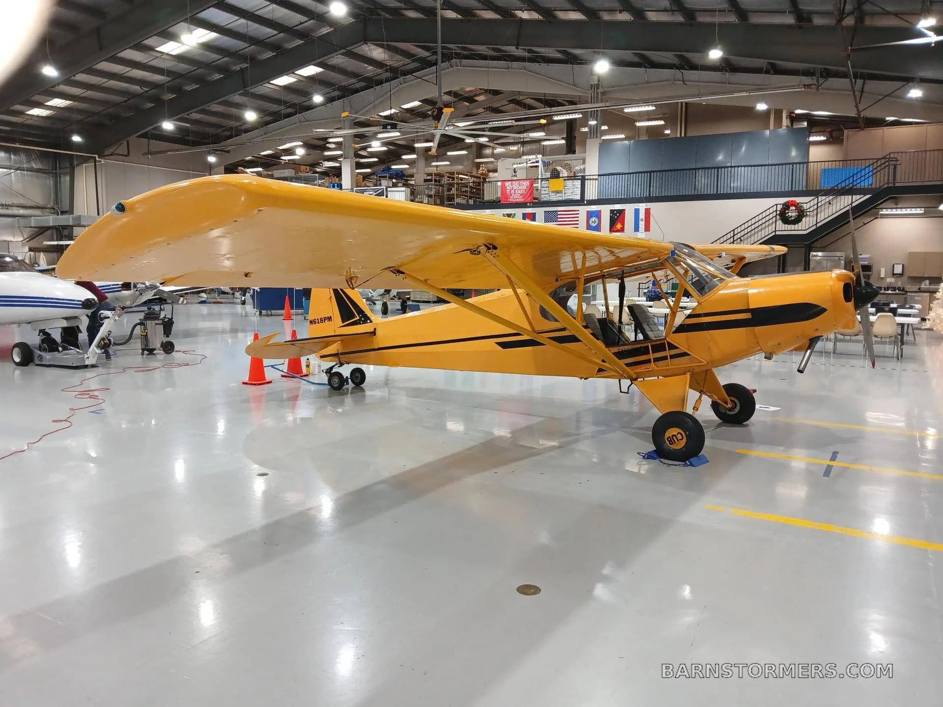 A yellow single-engine high-wing aircraft with black stripes, parked inside a hangar.