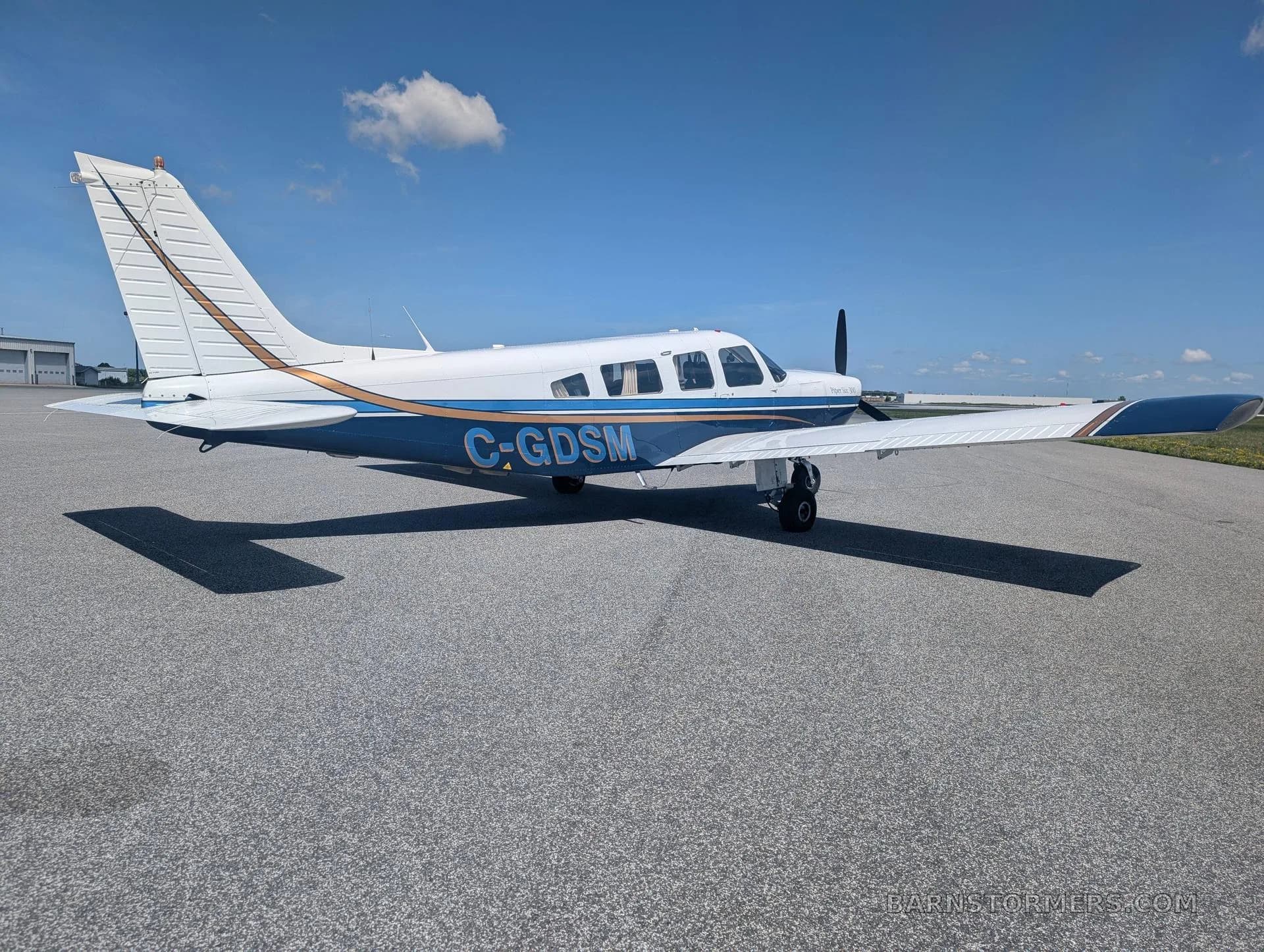A side view of a white and blue Piper Archer 200 aircraft with registration C-GDSM, parked on an asphalt tarmac.