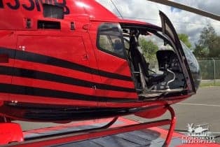 Close up of a red and black helicopter with the tail number N135MB with the door open.
