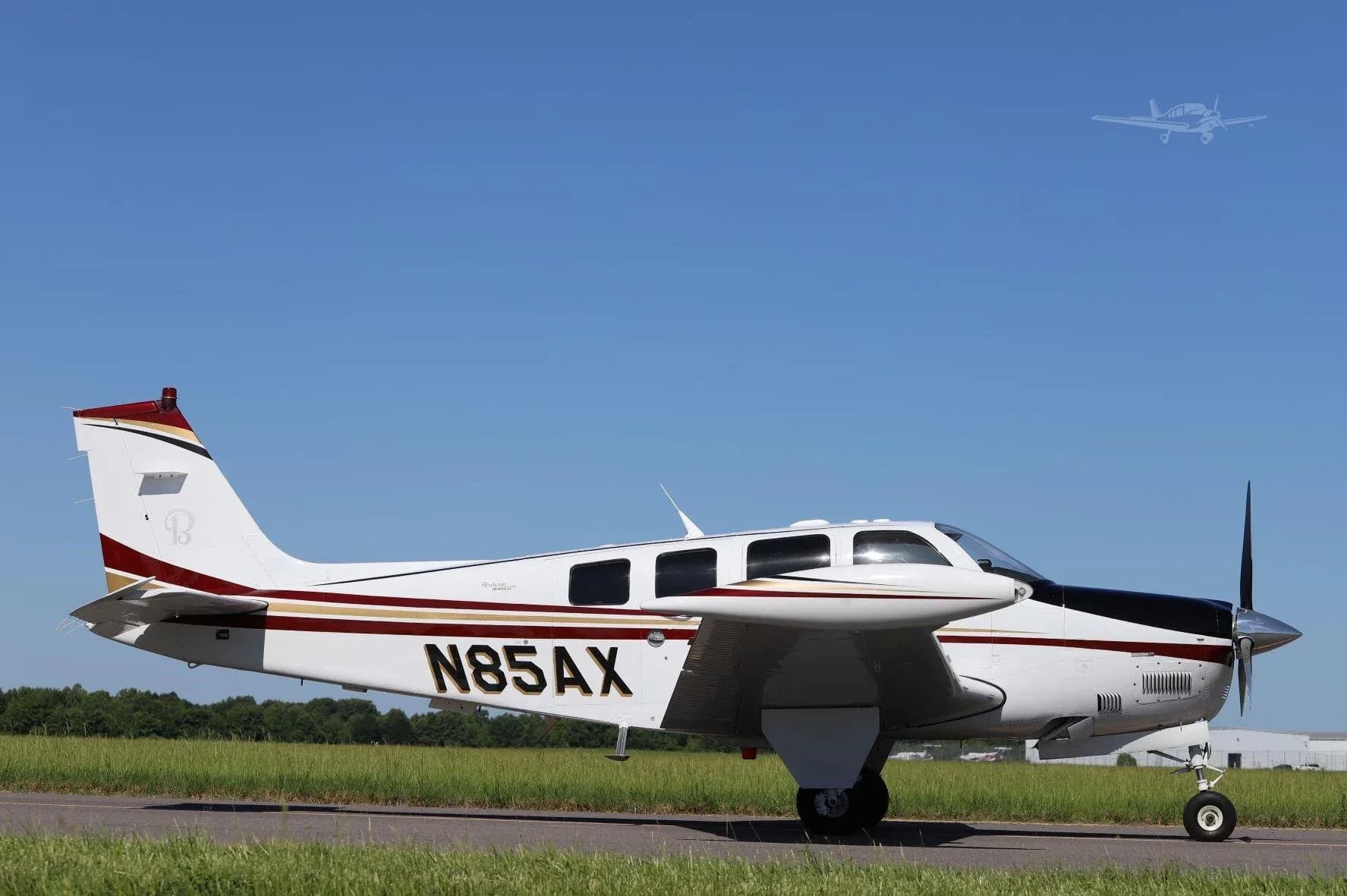 A white and black single-engine propeller aircraft with red and gold stripes and registration N85AX, viewed from the right side on a tarmac.