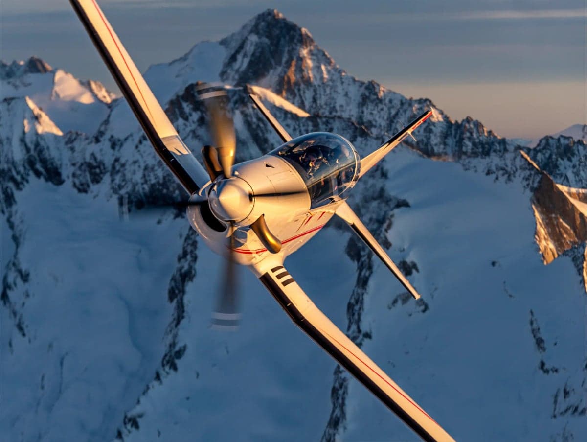 A Pilatus PC-7 MKX aircraft flying in front of a mountain range.
