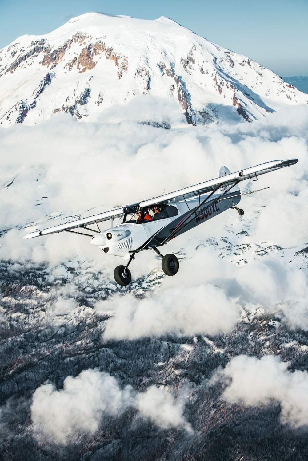 An XCub aircraft flies in front of a snow-covered mountain.