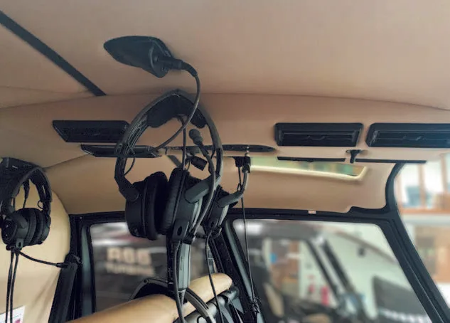 Black aviation headsets hang from the overhead panel inside a helicopter cabin.