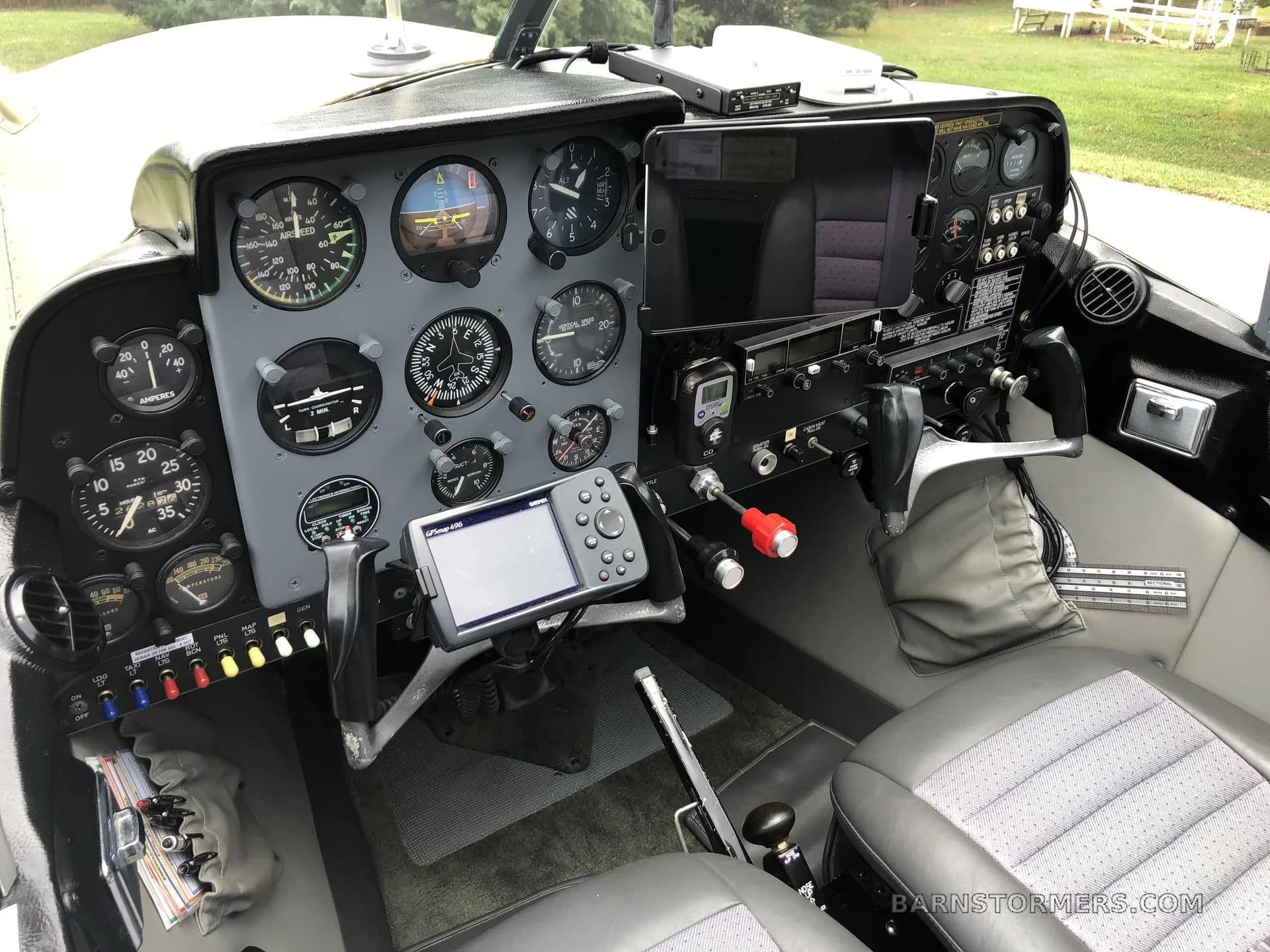 The cockpit of a small aircraft features a grey instrument panel with analog gauges and a modern GPS unit.