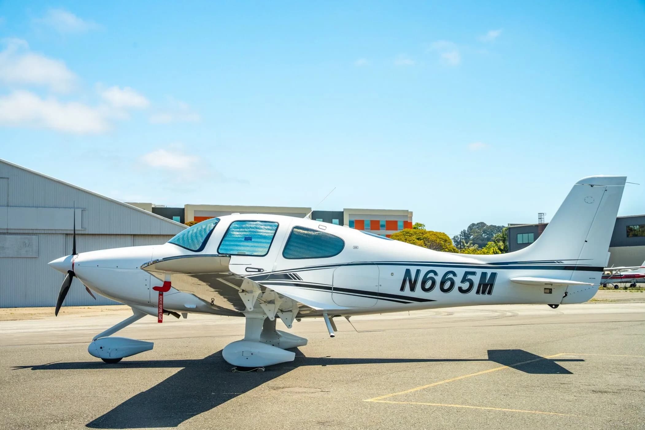 A white Cirrus SR22 aircraft with registration N665M parked on the tarmac with sun shades in the windows.