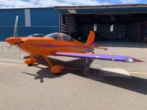 An orange and purple aircraft parked in front of a hangar.