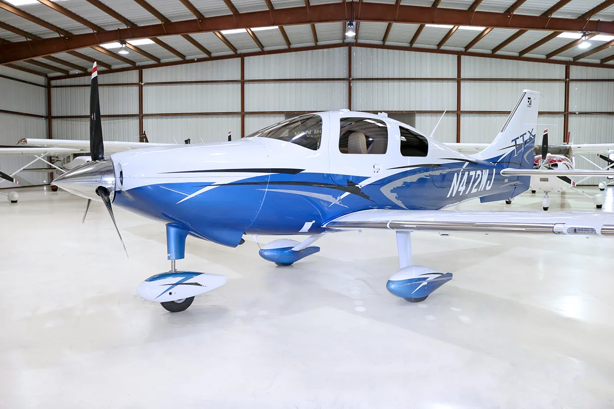 A white and blue Cessna TTx aircraft, registration N472WJ, is parked in a hangar, viewed from the front-left.