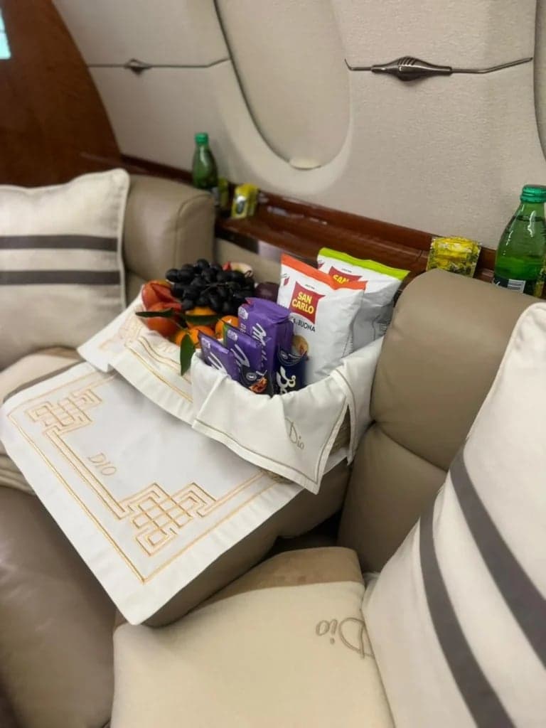 A close-up of a tray with snacks and drinks on a tan leather seat inside the aircraft.