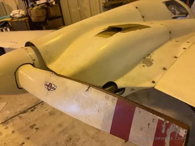 A close-up of the white pusher propeller and engine cowling of an experimental aircraft, showing red stripes on the propeller blades.
