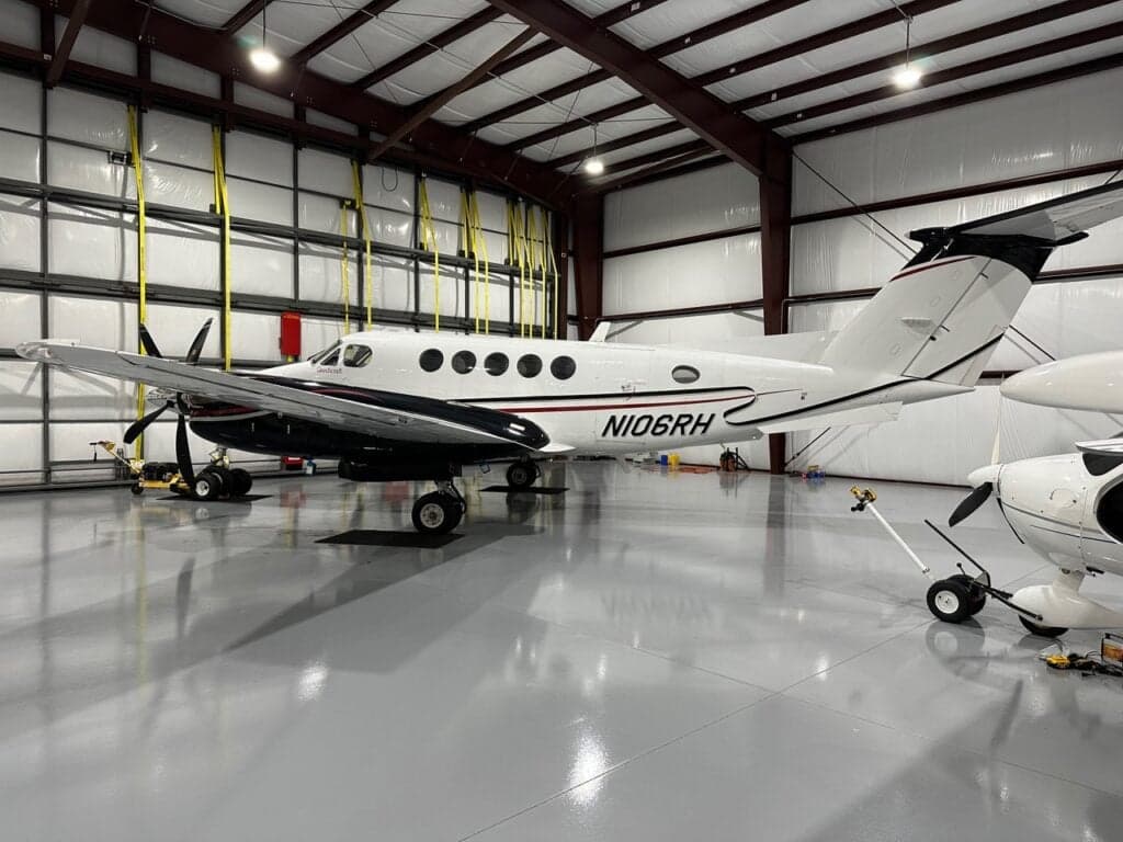 A full side view of the white Beechcraft King Air N106RH with black and red stripes, parked in a hangar.