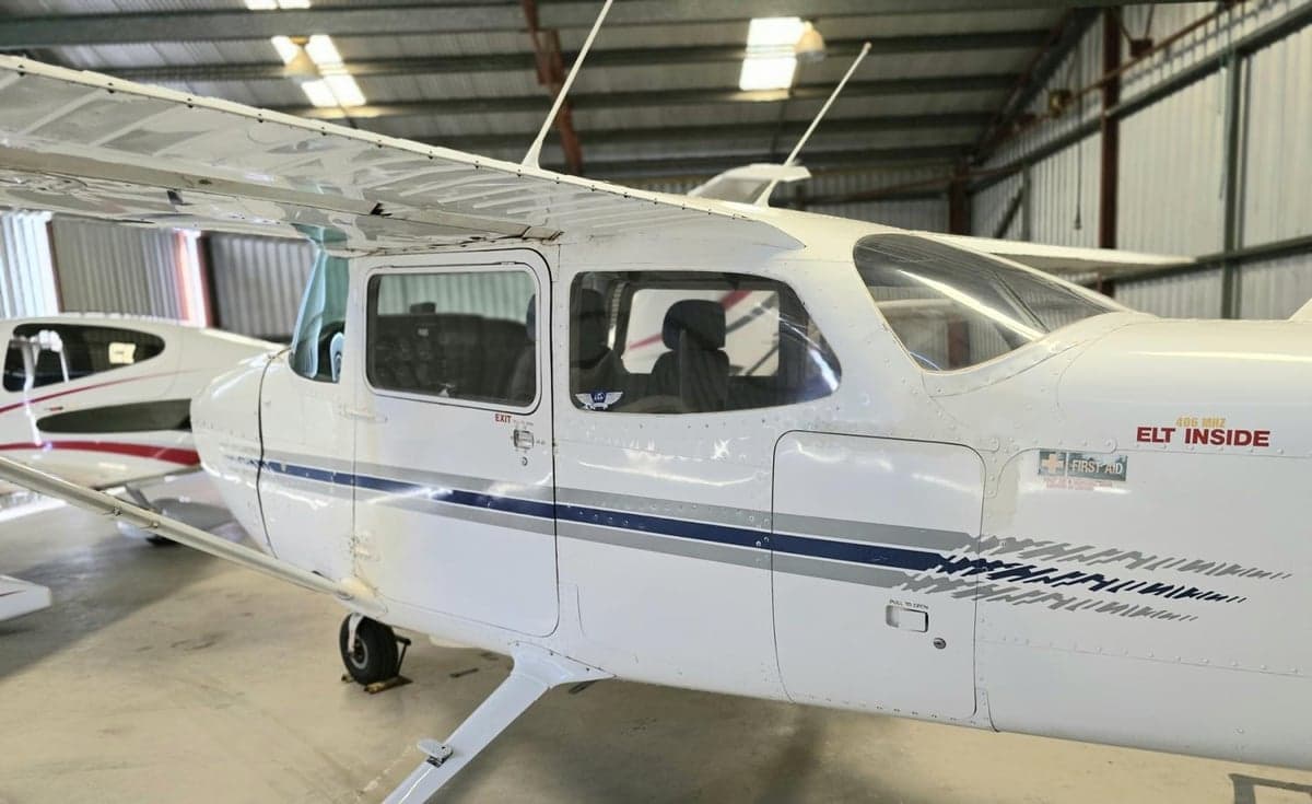 A Cessna aircraft is parked inside a hangar, showing the side and cabin windows.