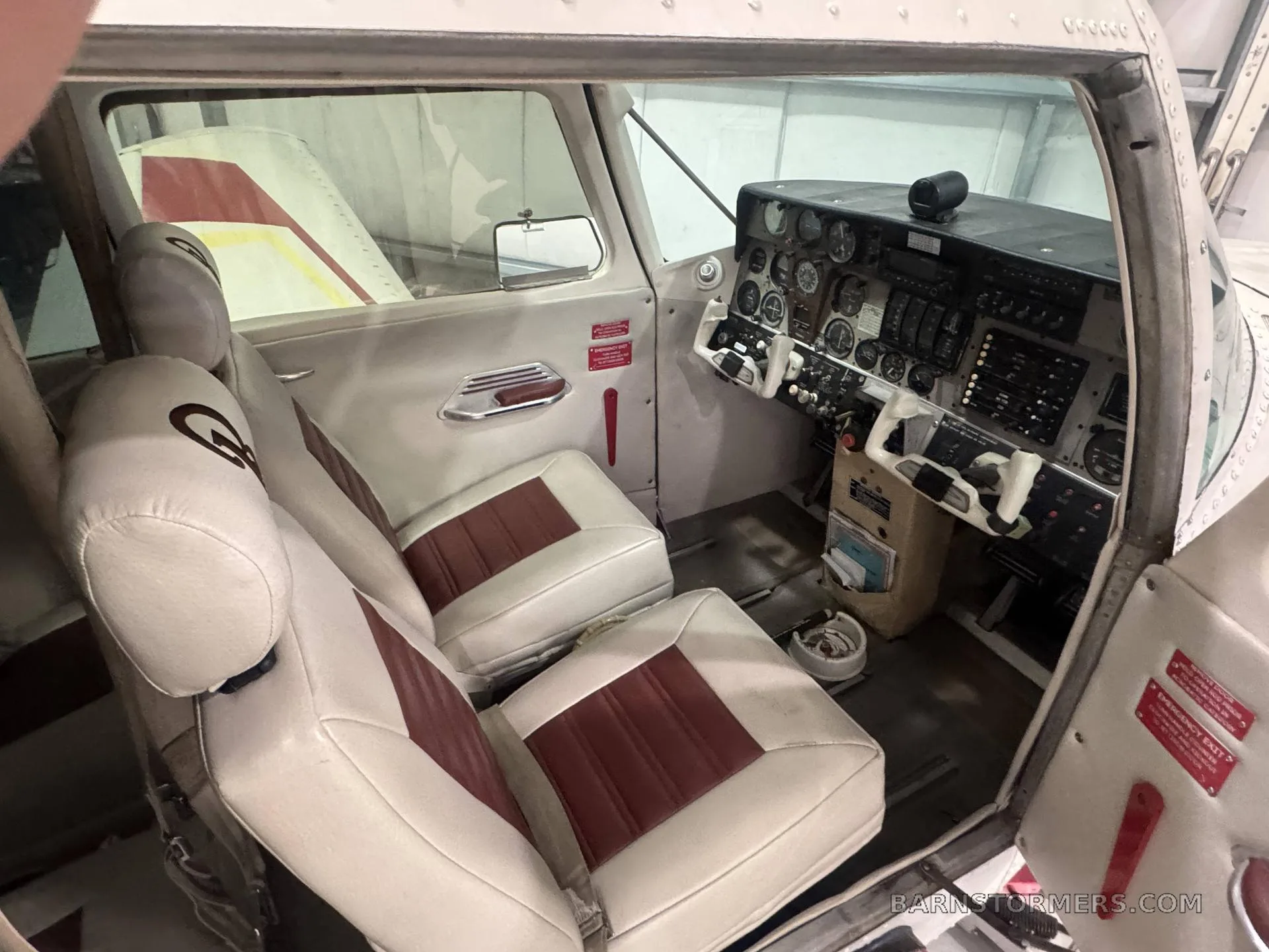 The interior of the aircraft shows white and red seats and the instrument panel on the right.