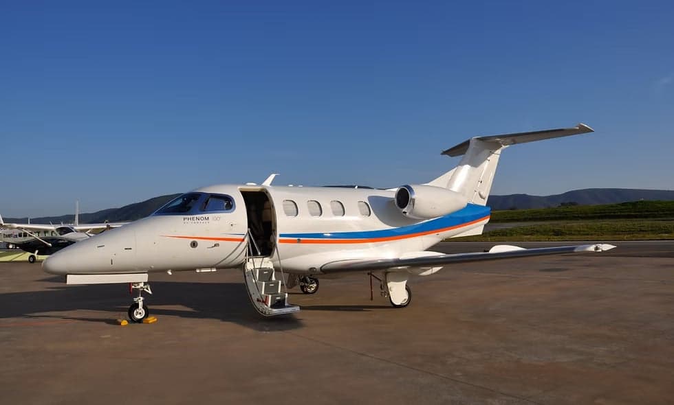A Phenom 300 aircraft parked on the tarmac with the door open.