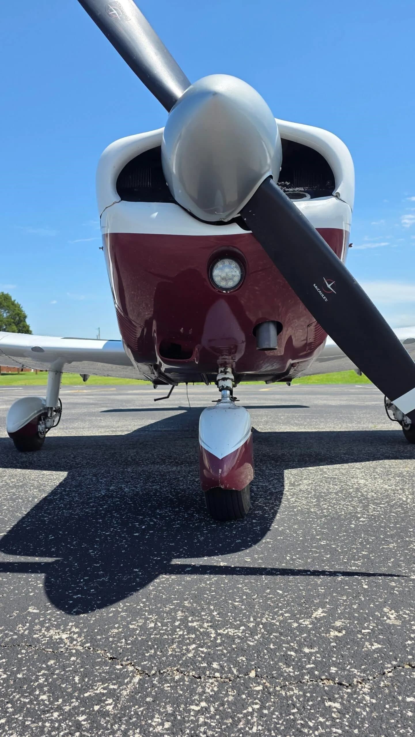 A very close-up view of the propeller, nose gear, and landing light of a white and maroon Piper Cherokee (N9221W).