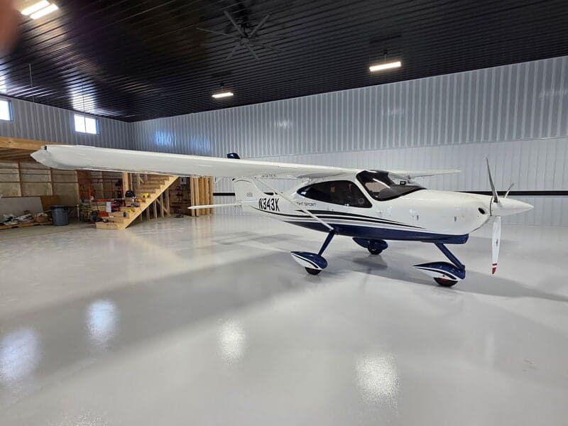 A white and blue Tecnam P2008 Light Sport aircraft (N343X) is parked in a hangar, showing a wider view of the interior.