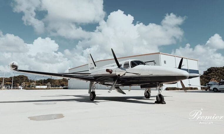 A twin-engine aircraft, N4938S, parked on the tarmac with a hangar in the background.
