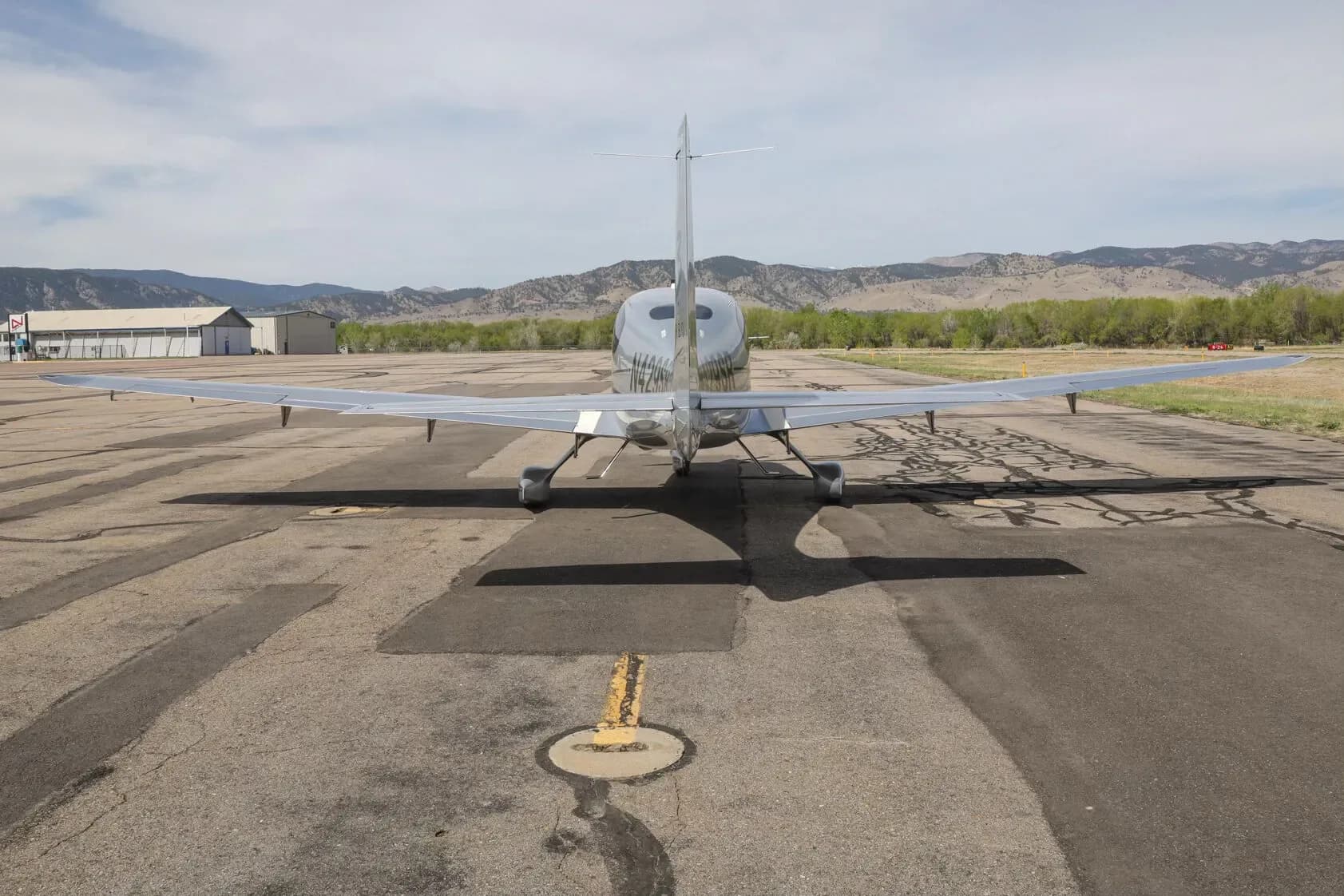 A silver Cirrus SR22T aircraft, registration N429SR, viewed from the rear, parked on an airfield with mountains in the background.