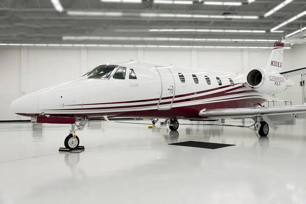 A white Cessna Citation XLS private jet with a maroon stripe and registration N301LG is parked in a brightly lit hangar, viewed from the front-left.