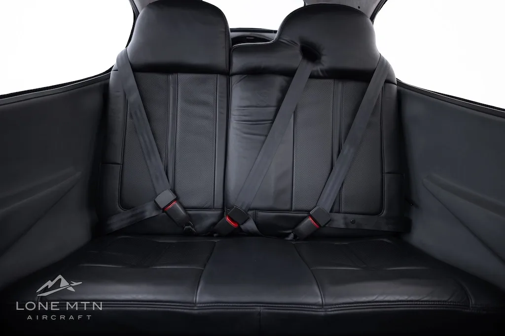 A straight-on view of the black leather rear seats of the aircraft cabin.