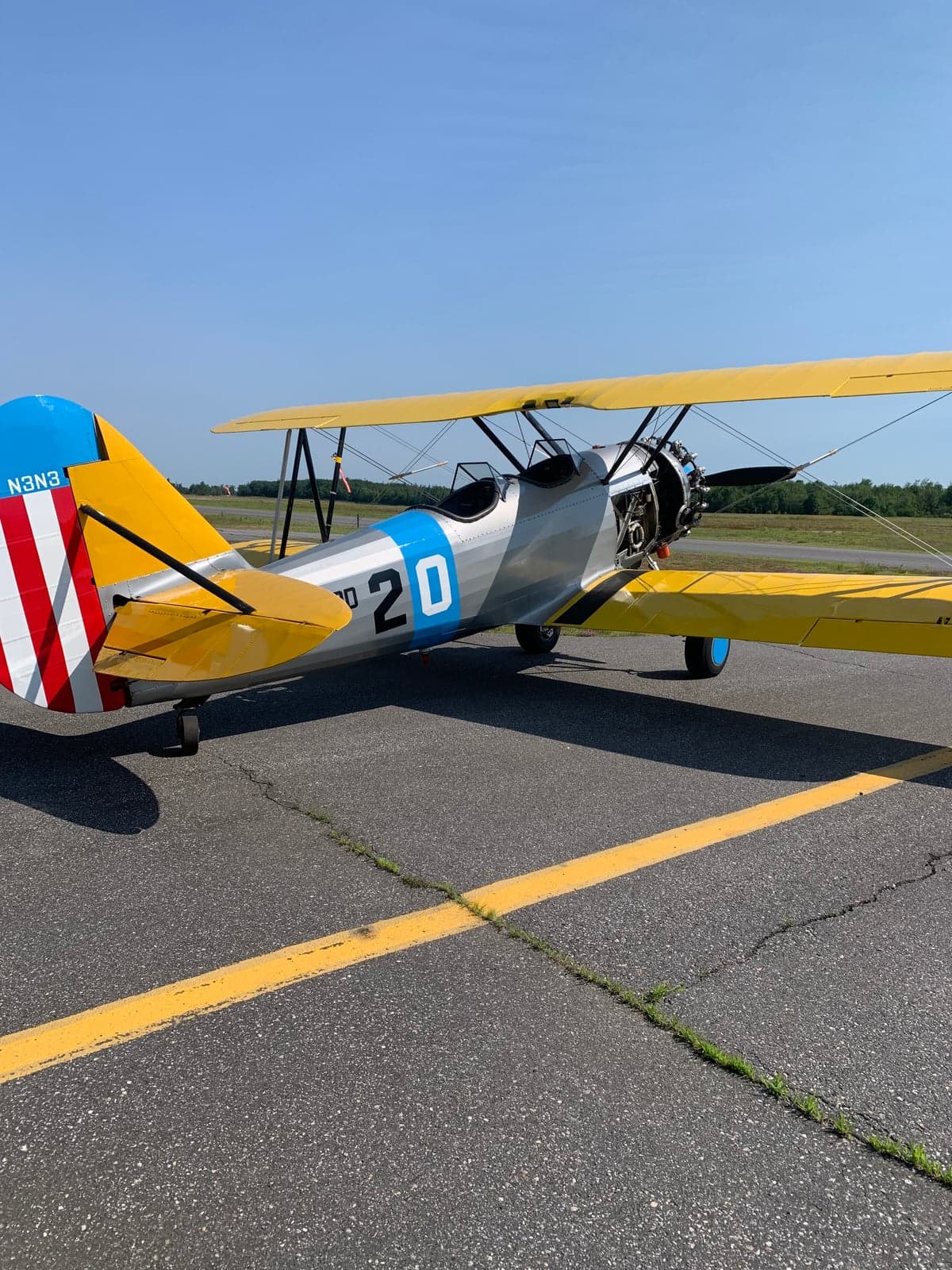 A yellow and silver biplane sits on the tarmac on a sunny day.