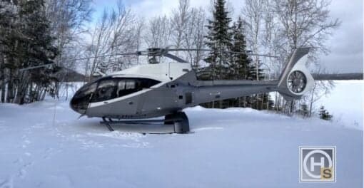 A grey and white helicopter, C-FTIT, parked in the snow near a lake.