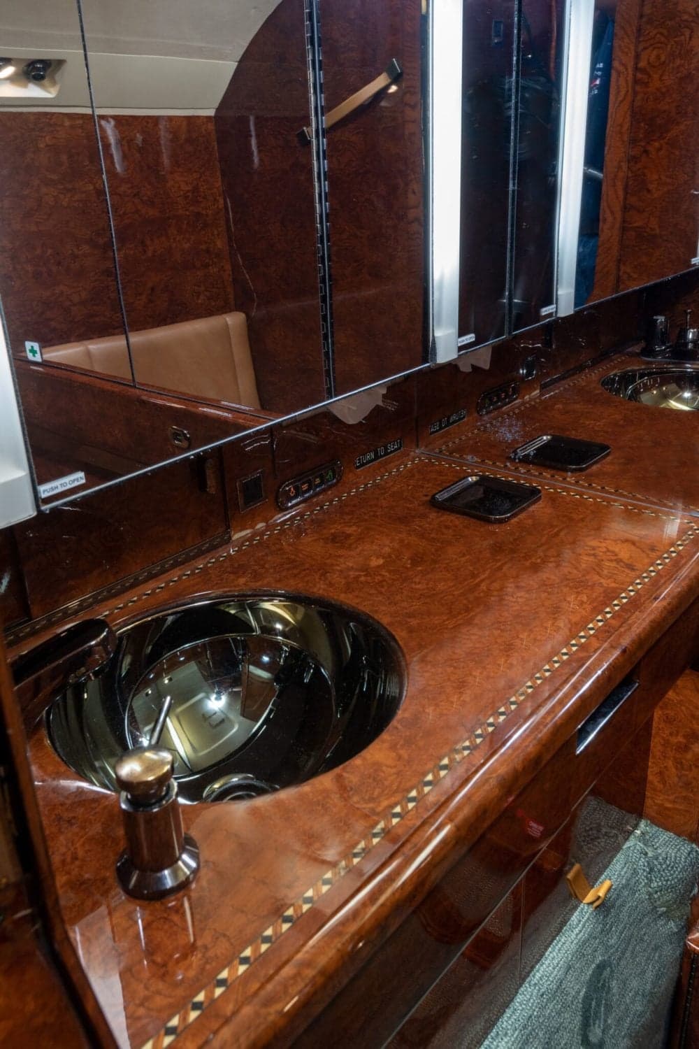 A close-up view of an aircraft lavatory or galley counter with a polished sink and rich wood paneling.