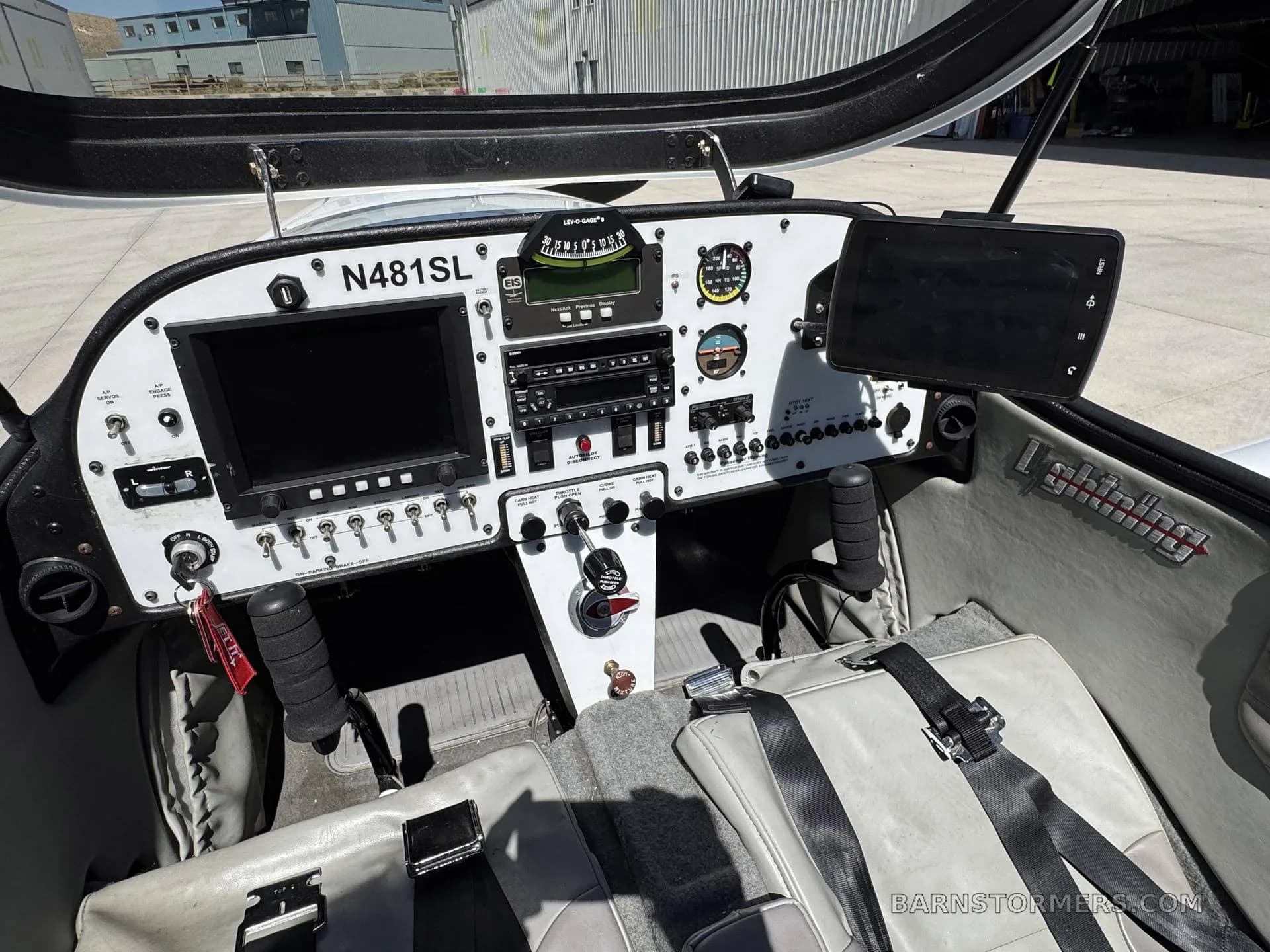The cockpit of a light aircraft, showing the instrument panel with dual screens and gray seats.