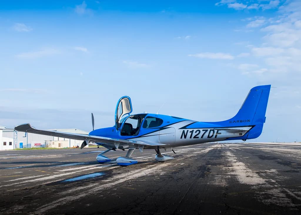 A blue and silver Cirrus SR22T GTS Carbon aircraft (N127DF) with its doors open, parked on a wet tarmac.