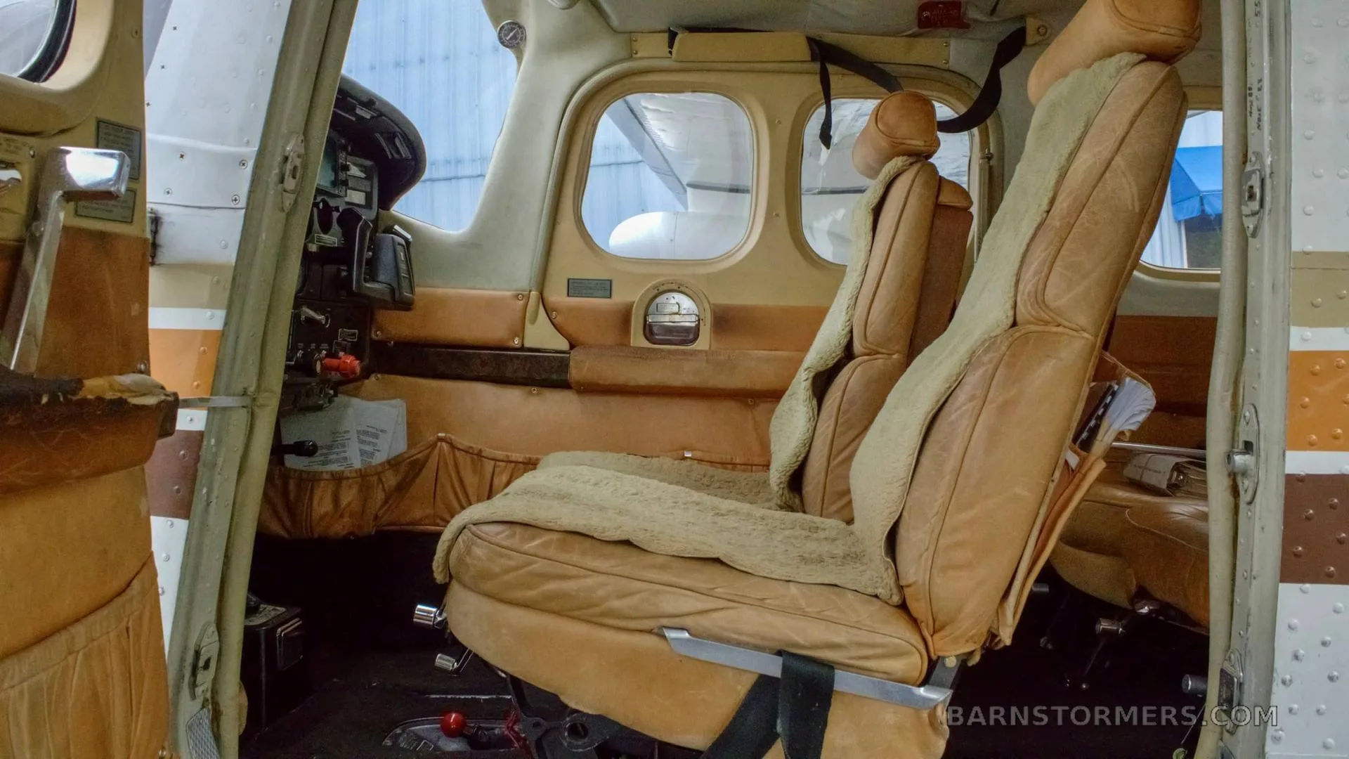 The aircraft's interior features tan leather seats with sheepskin covers and a view into the cockpit.