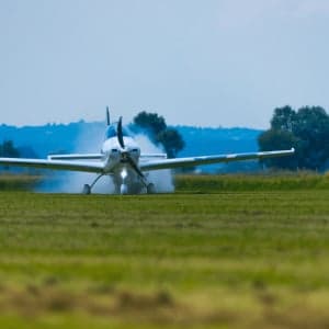 A white aircraft lands on a grassy runway.