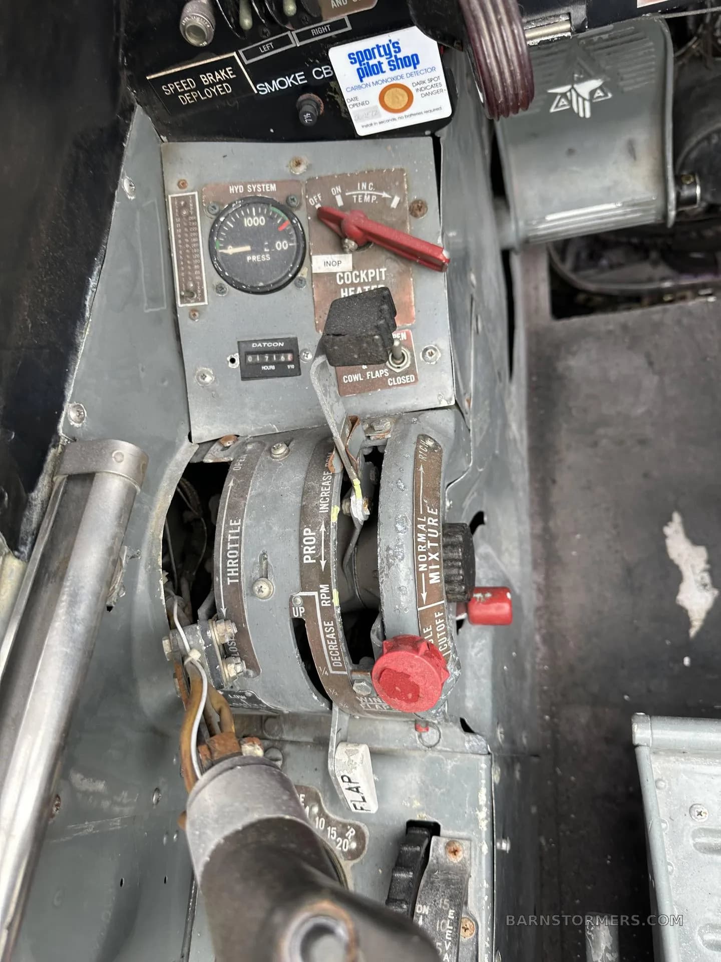 A close-up view of the throttle, propeller, and mixture controls, along with other switches, in a vintage aircraft cockpit.