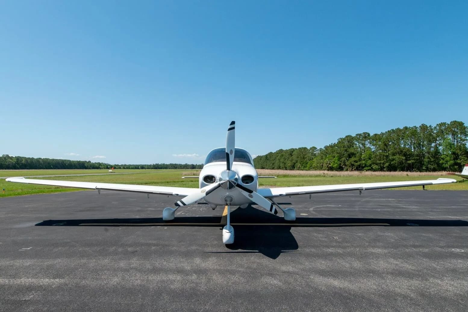 Front view of a white Cirrus SR22T aircraft N717PG with a three-bladed propeller on an airfield.