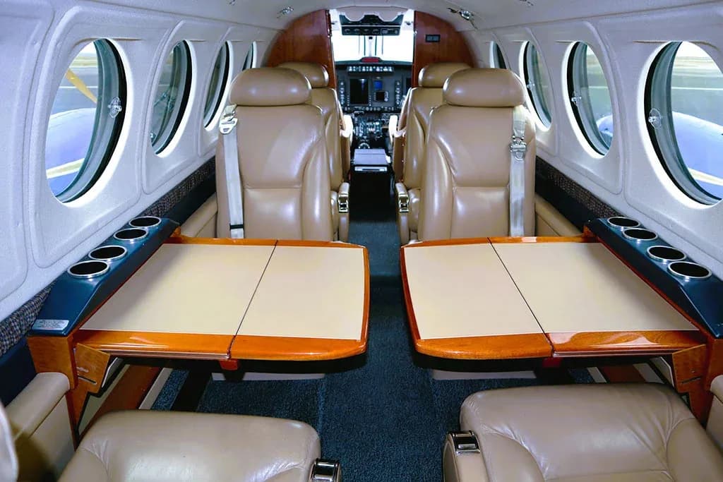 The aircraft cabin interior featuring tan leather seats and two fold-out tables in a club seating arrangement.
