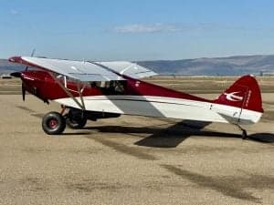 Side view of a red and white Carbon Cub aircraft on the ground.